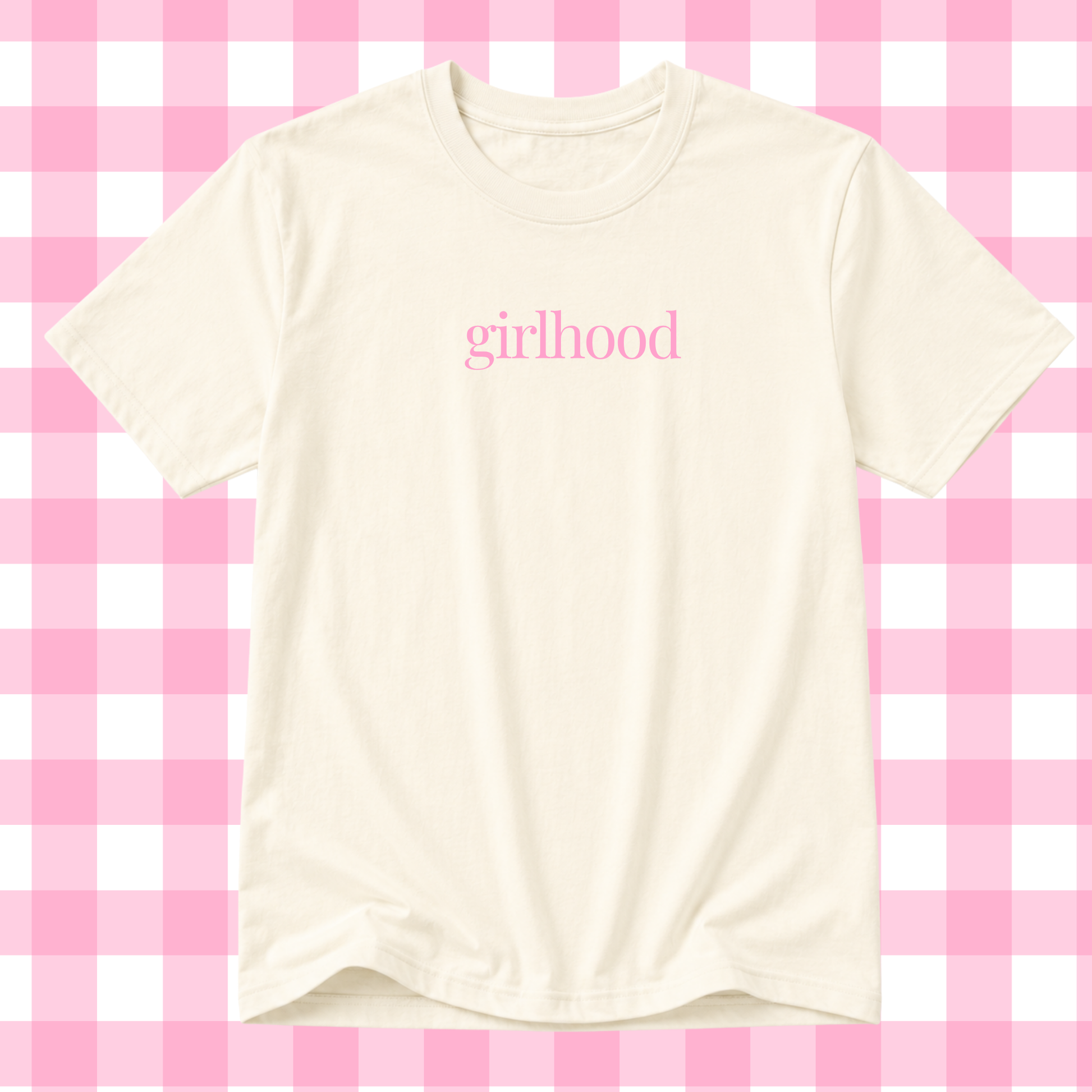 An off-white short-sleeve t-shirt with the word 'girlhood' printed in pink lowercase serif letters across the chest, displayed against a pink and white checkered background.
