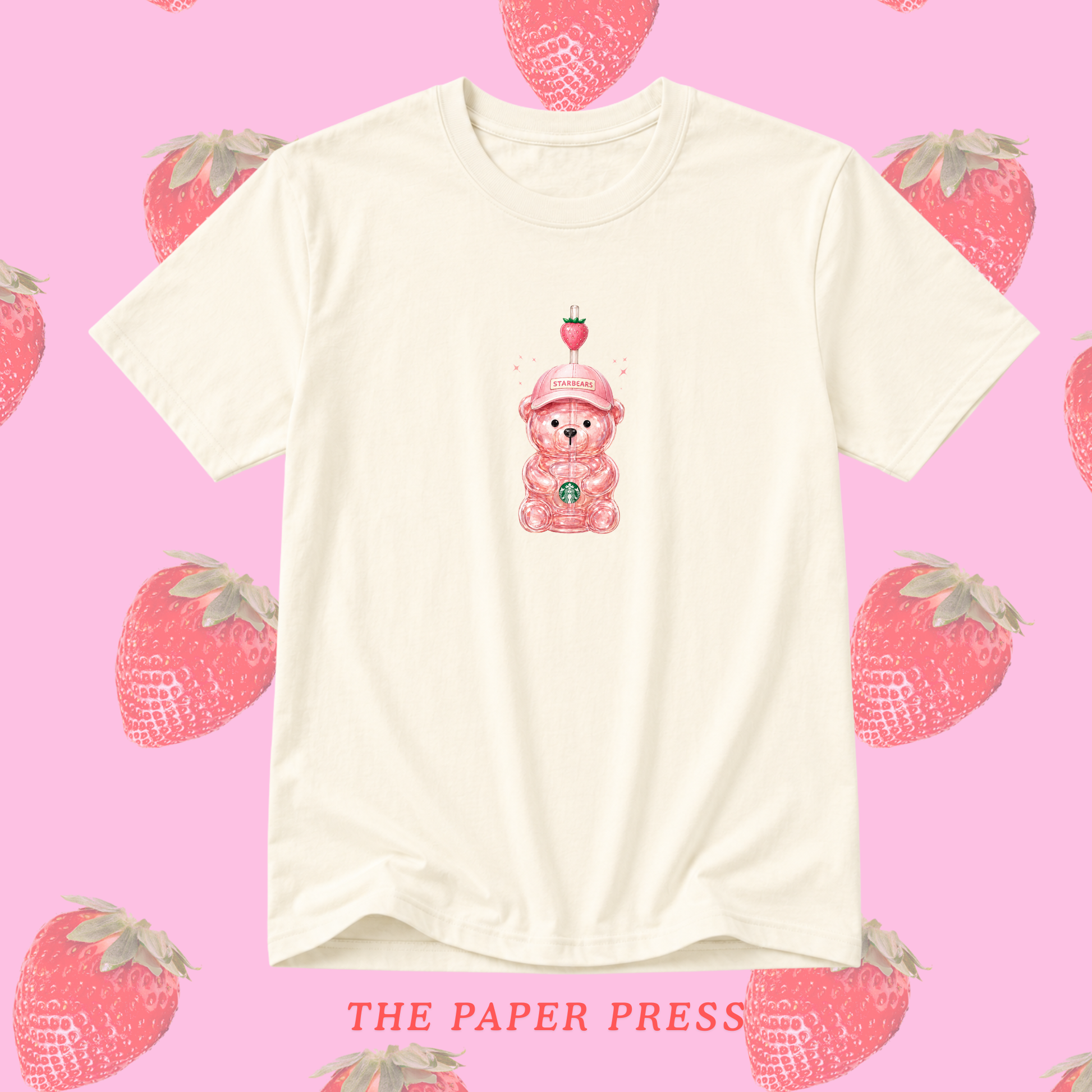 An off-white short-sleeve t-shirt with a cute pink teddy bear wearing a strawberry hat graphic on the chest, displayed against a pink background patterned with strawberries. The text 'THE PAPER PRESS' is visible at the bottom.