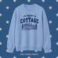 Heated Rivalry coded sweatshirt featuring “I’m Coming to the Cottage” collegiate-style text with a detailed cottage and pine tree illustration, hand-printed by The Paper Press.