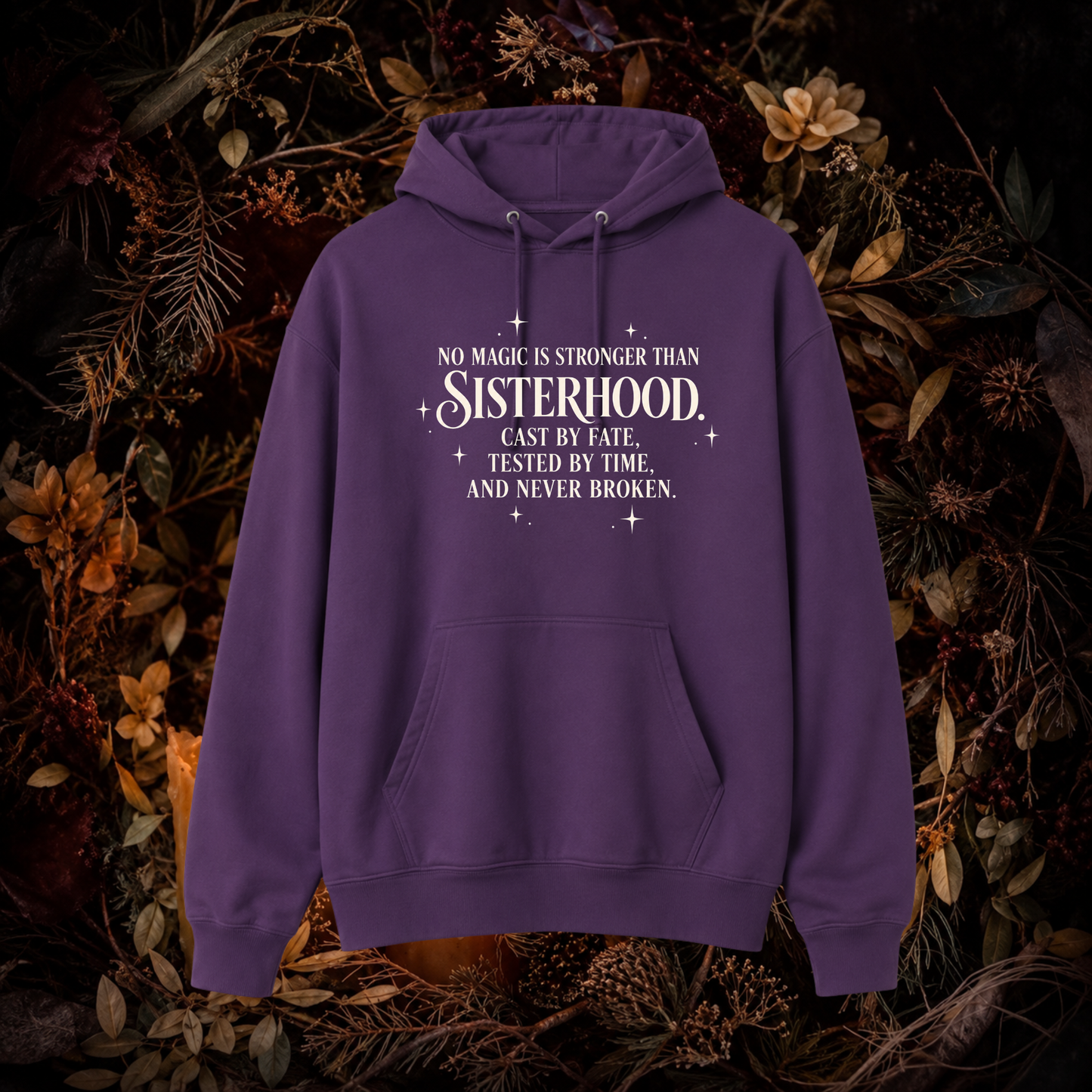 A purple pullover hoodie with a white printed quote on the chest, displayed against a dark background of dried flowers and foliage.
