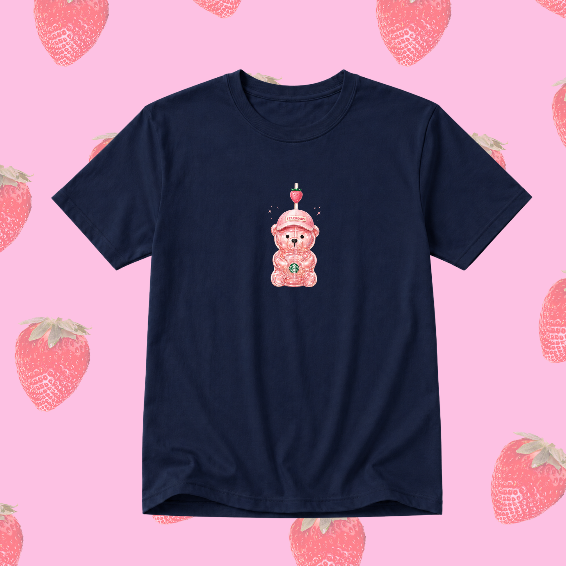 A navy blue short-sleeve t-shirt featuring a cute graphic of a pink teddy bear wearing a party hat with a candle. The t-shirt is displayed against a pink background patterned with illustrated strawberries.