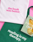 White shirt with 'the book was better' text, green tote bag with 'reading is my therapy' text, and book titled 'Finding Eden' on a pink background.