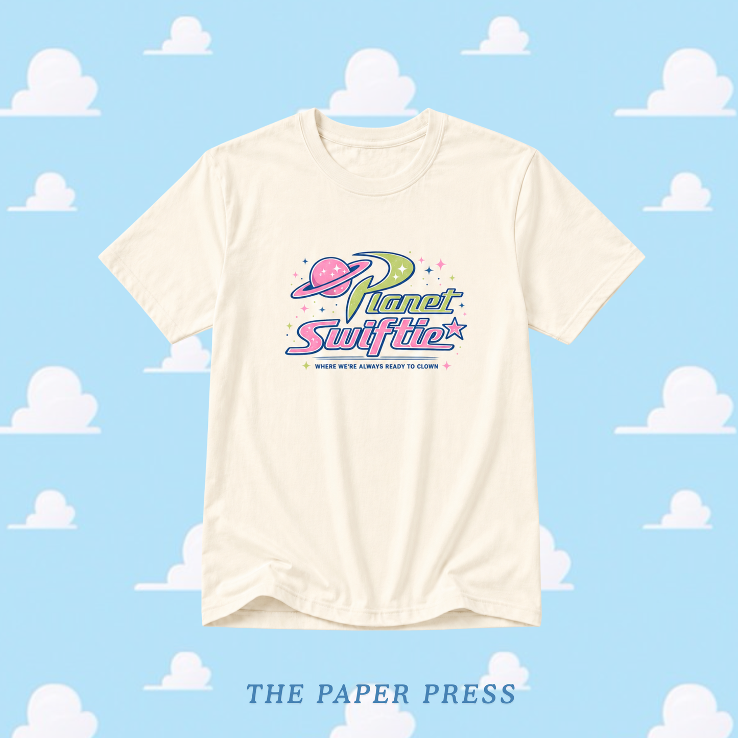 Beige t-shirt with 'Planet Swiftie' logo on a blue background with cloud patterns, featuring 'The Paper Press'.