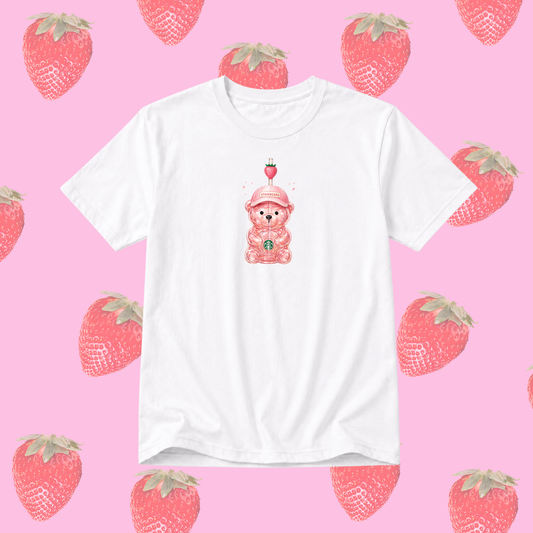 A white short-sleeve crewneck t-shirt featuring a cute pink bear graphic wearing a strawberry hat, centered on a pink background patterned with watercolor-style strawberries.