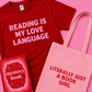 Red t-shirt with 'Reading is my love language' text, pink tote bag with 'Literally just a book girl' text, and red book with 'mystery book' text on a pink background.