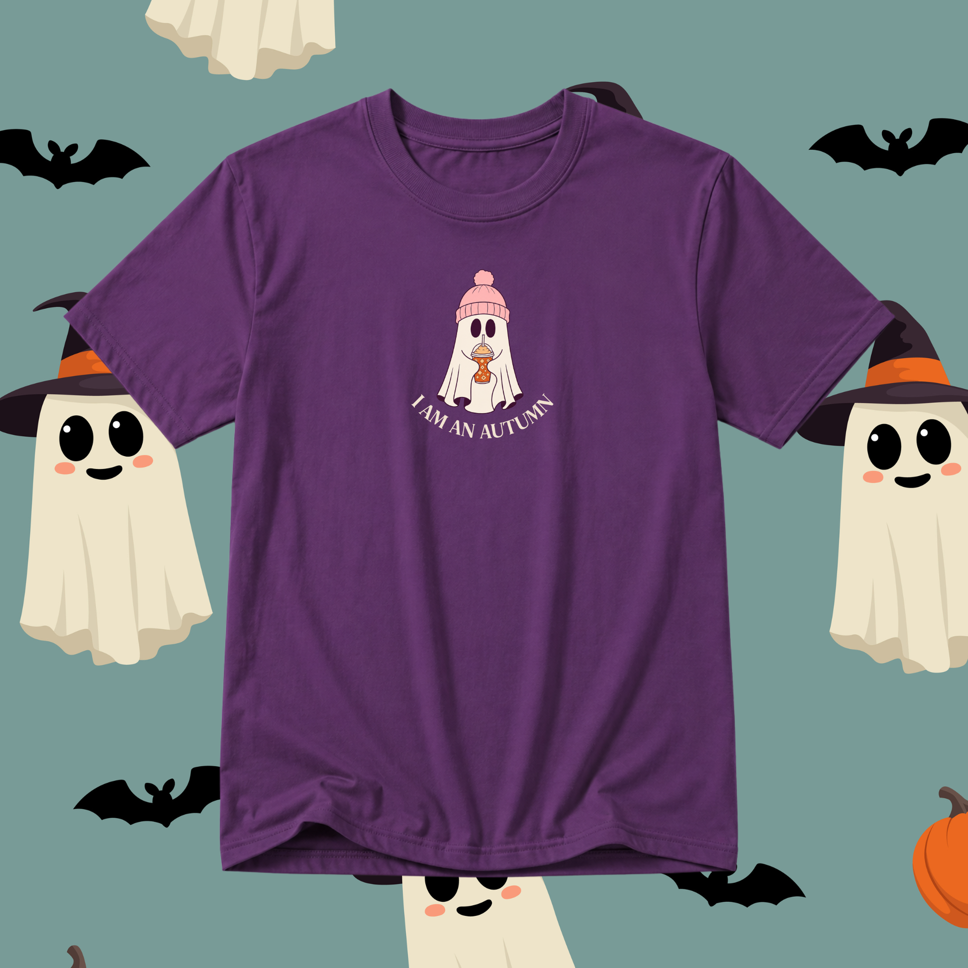 A purple short-sleeve t-shirt with a cute cartoon graphic of a ghost wearing a pink beanie and holding an autumn leaf, with the text 'I AM AN AUTUMN' below it. The t-shirt is displayed against a teal background decorated with Halloween-themed illustrations including ghosts, bats, and an orange pumpkin.