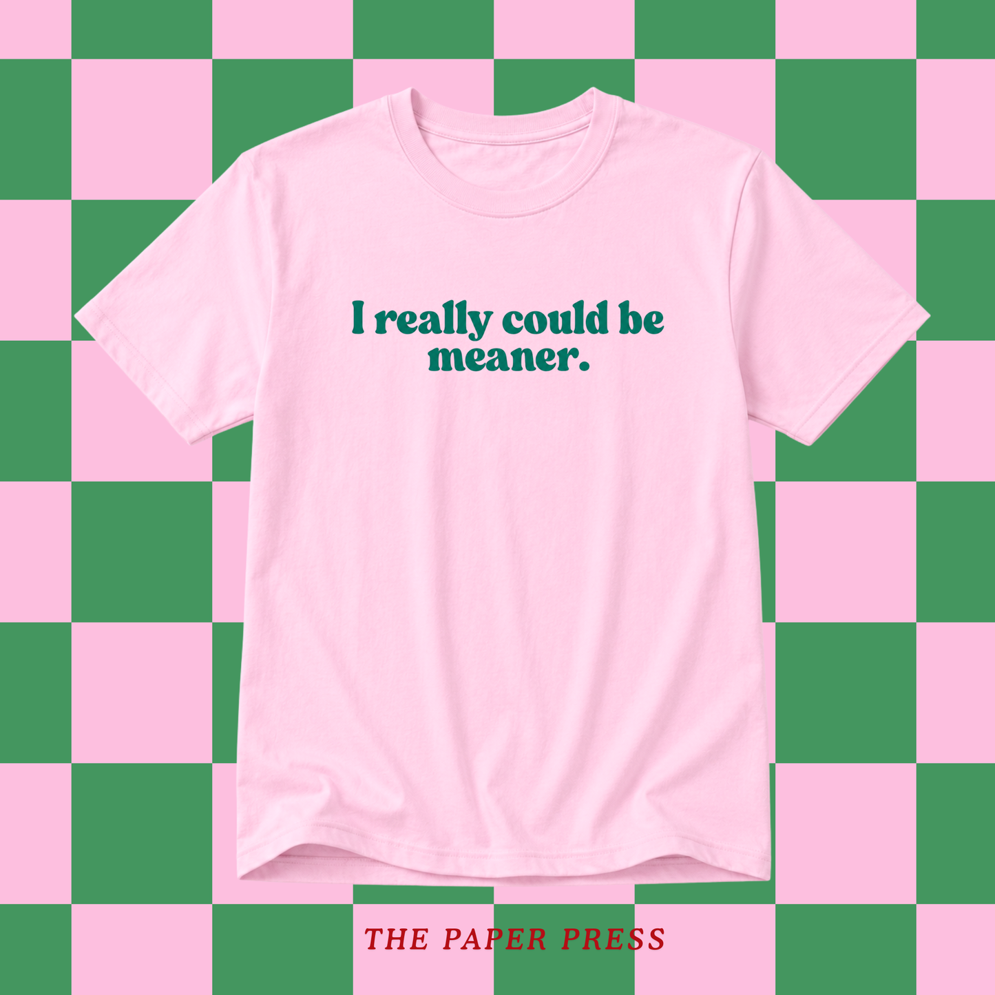 A light pink short-sleeve t-shirt with the text 'I really could be meaner.' printed in dark teal across the chest, displayed against a pink and green checkered background.
