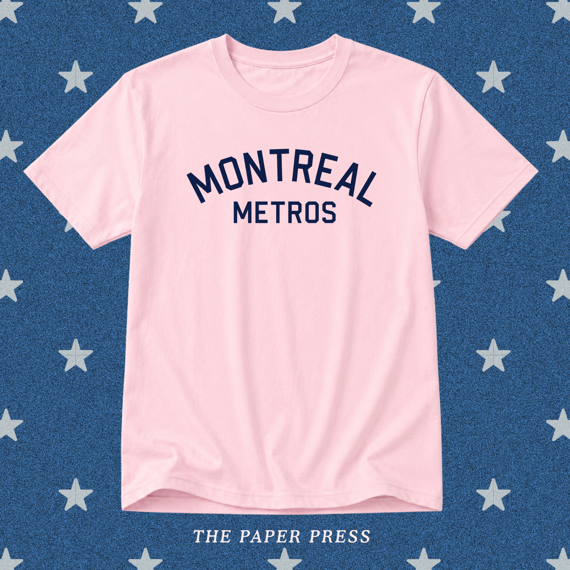 A light pink short-sleeve t-shirt with 'MONTREAL METROS' printed in navy blue arched text on the chest, displayed flat against a blue background patterned with white stars. 'THE PAPER PRESS' is printed at the bottom.