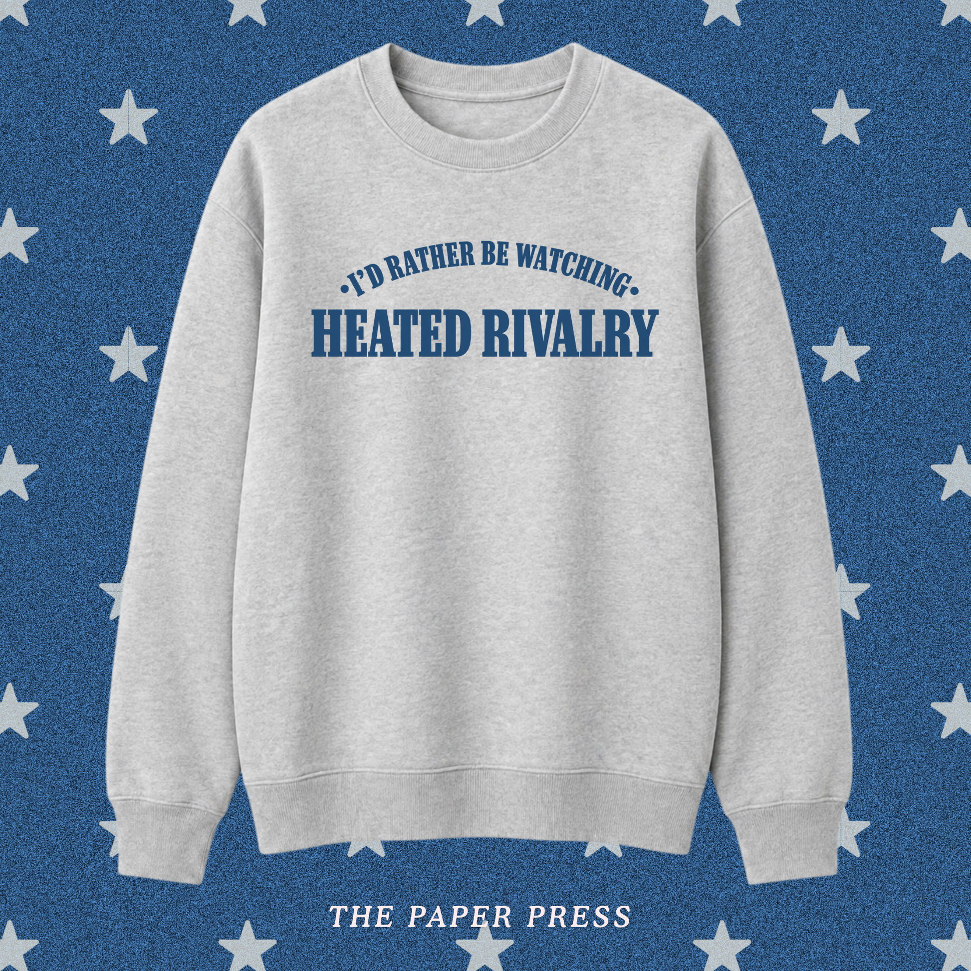 A light heather gray crewneck sweatshirt with blue text reading 'I'D RATHER BE WATCHING HEATED RIVALRY' on the chest, displayed against a blue background with white stars and the text 'THE PAPER PRESS' at the bottom.