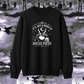 A black crewneck sweatshirt with a white graphic print reading 'IT'S JUST A BUNCH OF HOCUS POCUS' around an illustration of a cauldron, skull, and crescent moon. The sweatshirt is displayed against a spooky Halloween graveyard background with tombstones, crows, and full moons.