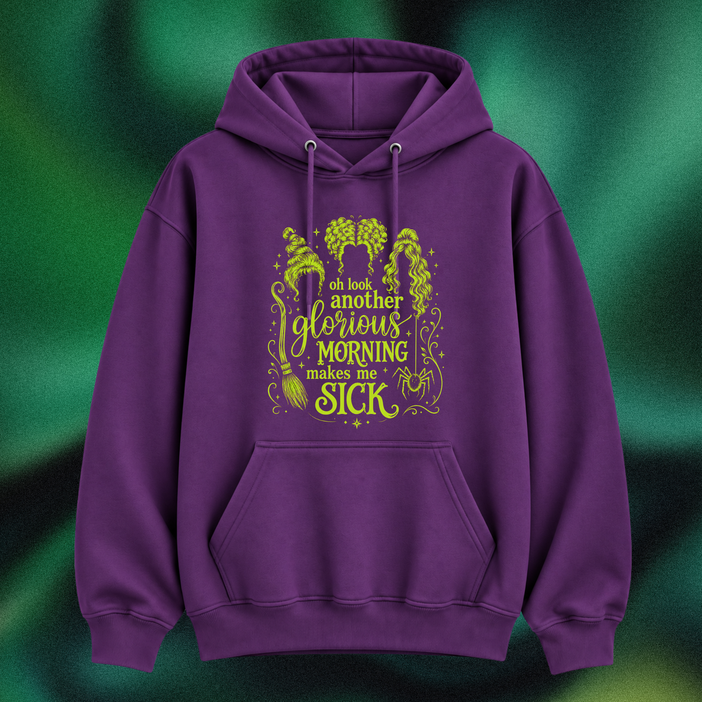 A purple pullover hoodie with a green graphic print on the front, featuring the text 'oh look another glorious MORNING makes me SICK' with witch illustrations, shown against a dark green textured background.