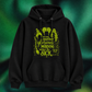 A black pullover hoodie with a vibrant lime green graphic on the front featuring the text 'oh look another glorious MORNING makes me SICK' surrounded by witchy illustrations like cauldrons, broomsticks, and a pentagram. The hoodie is displayed against a dark green, textured, smoky background.