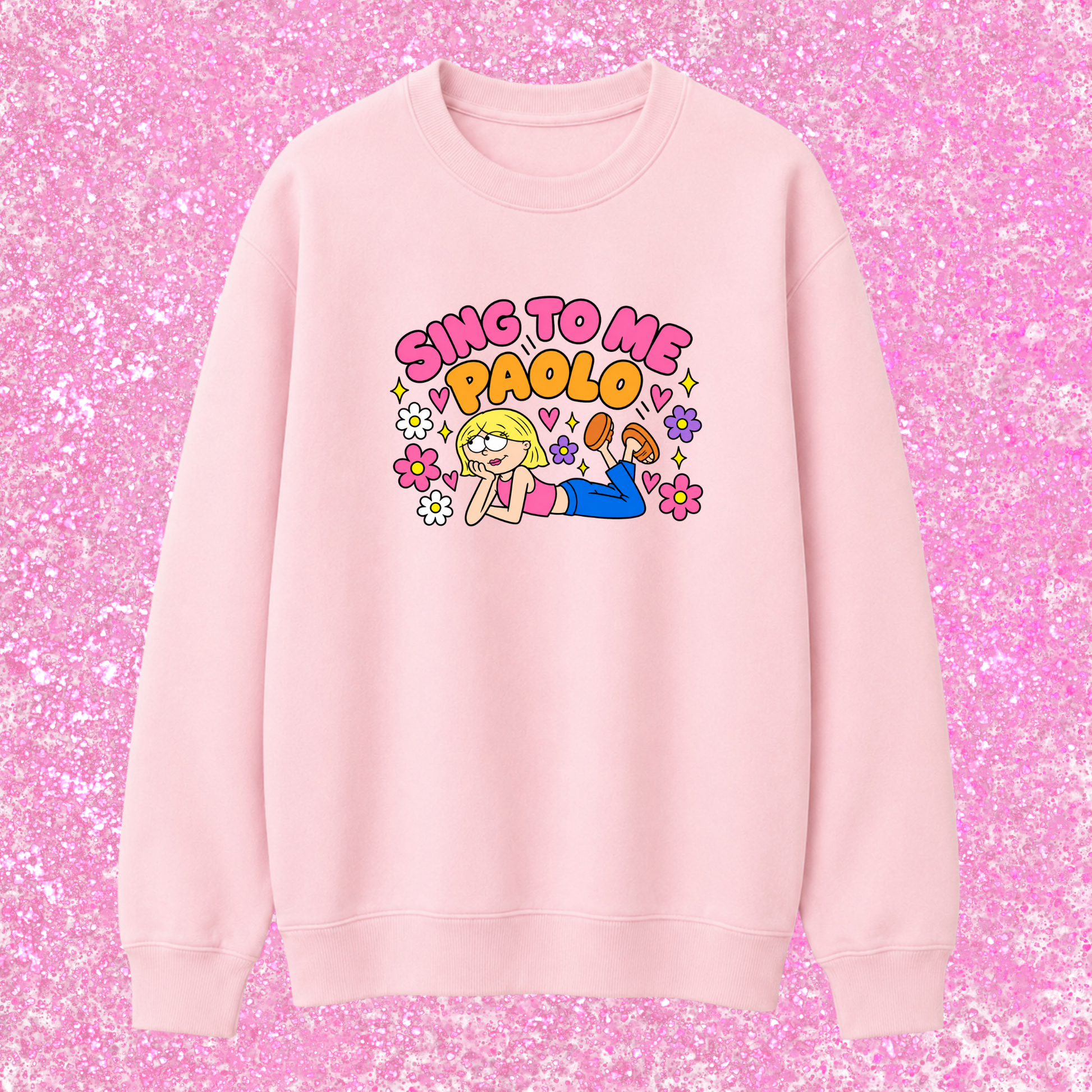 A light pink crewneck sweatshirt featuring a colorful graphic of a cartoon girl and the text 'SING TO ME PAOLO' in pink and yellow, displayed against a pink glitter background.