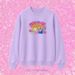 A lavender crewneck sweatshirt featuring a colorful graphic of a cartoon girl and the text 'SING TO ME PAOLO' in pink and yellow, displayed against a pink glitter background with 'THE PAPER PRESS' text at the bottom.